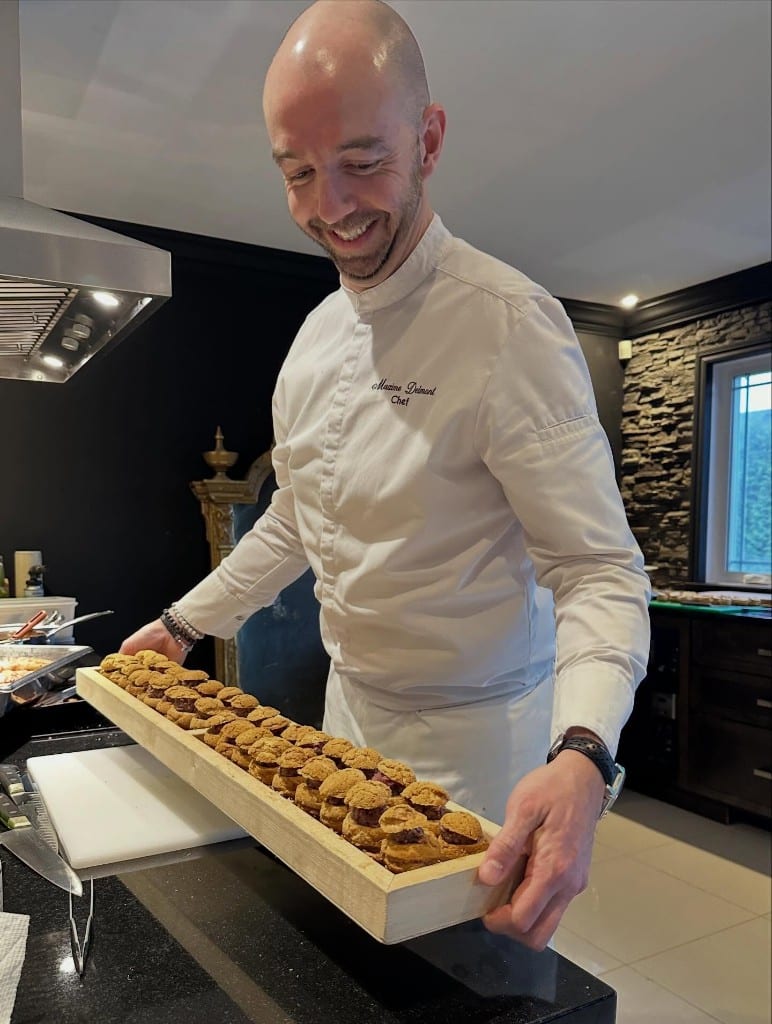 Chef Max Delmont souriant, tenant un plateau de sandwiches lors d’une prestation à Laval